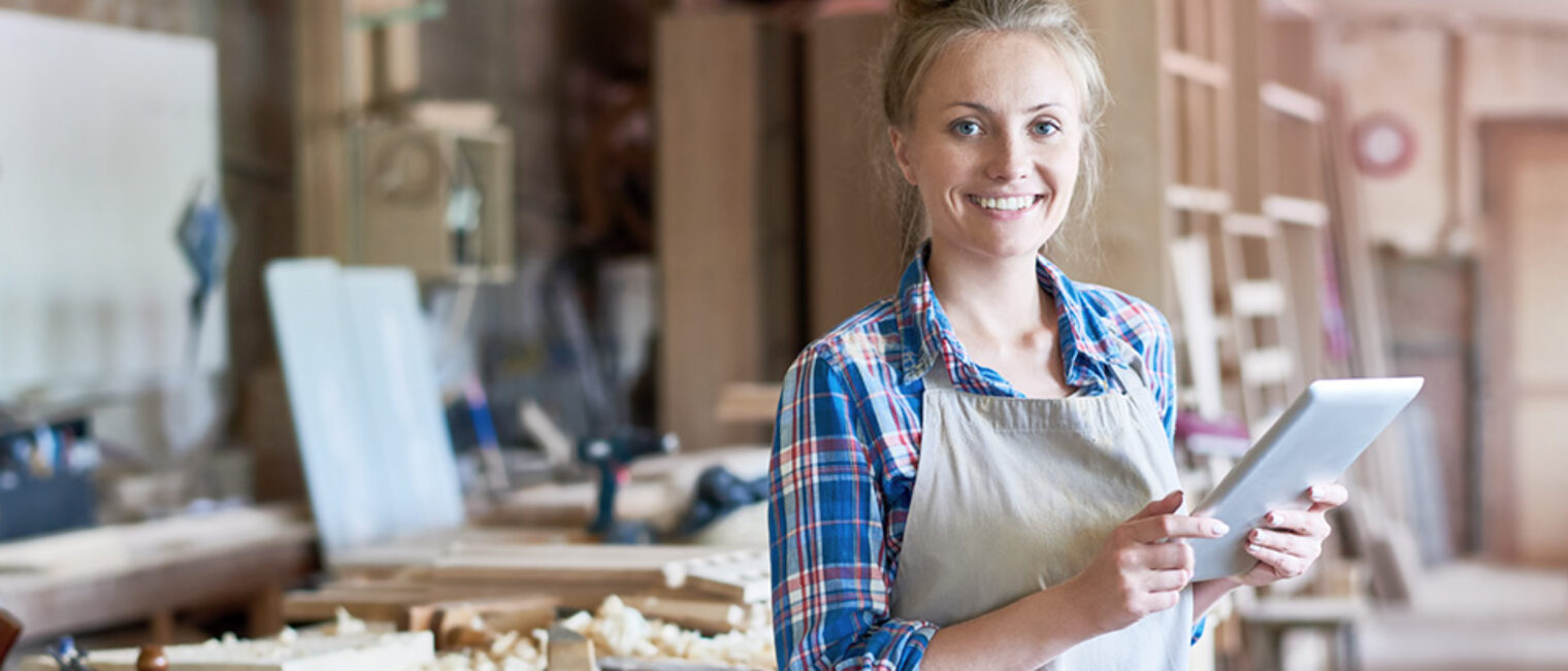 Portrait of happy young woman looking at camera using digital tablet in modern woodworking shop, copy space Schlagwort(e): small, business, traditional, craft, wood, wooden, woodwork, carpenter, carpenting, carpentry, joiner, joinery, manufactory, manufacturing, occupation, modern, workshop, work, shop, young, woman, female, using, digital, tablet, technology, connectivity, looking, camera, smiling, happy, manager
