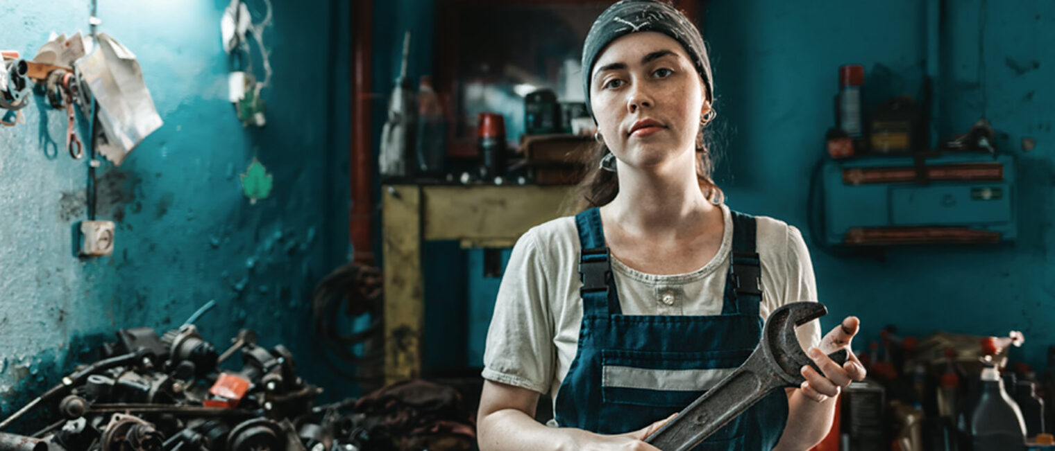 The concept of small business, feminism and women's equality. A young woman in overalls poses with a large wrench in her hands. Schlagwort(e): woman, auto, mechanic, wrench, garage, feminism, business, service, work, factory, technician, car, profession, equality, engine, spare parts, diagnostic, worker, industry, auto repair shop, hobby, occupation, tool, employment, workshop, holding, female, automotive, concept, engineer, mechanical, protection, lifestyle, technique, young, equipment, inspection, transportation, transport, success, safety, apprentice, shop, diy, electronic, vehicle, job, land vehicle, robe, indoors