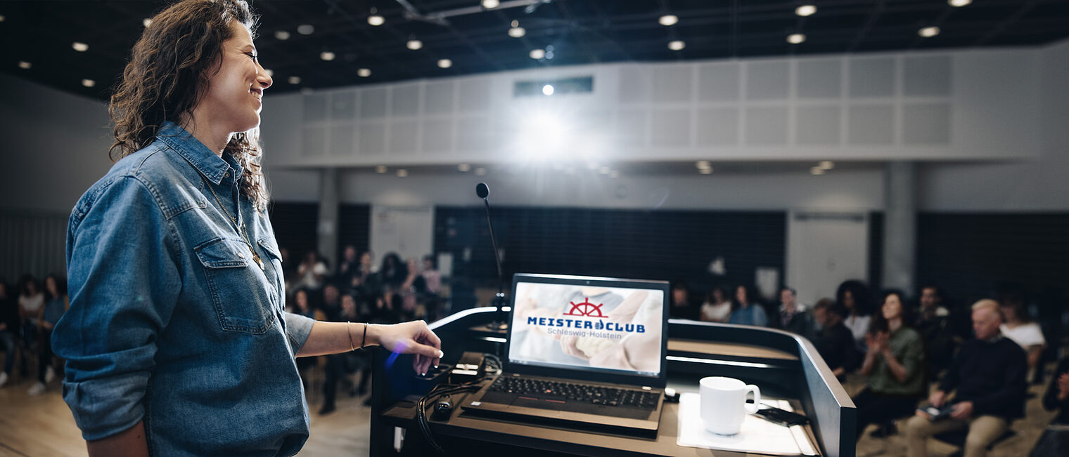 Wide angle shot of a female speaker standing at podium with laptop on the lectern and people sitting in the auditorium. Businesswoman giving a presentation in a corporate event. Schlagwort(e): audience, auditorium, background, business, businesswoman, convention, copy space, corporate, entrepreneur, forum, happy, meeting, office, people, podium, presentation, presenter, profession, professionals, public, rear, seminar, speaker, speech, view, woman, worker