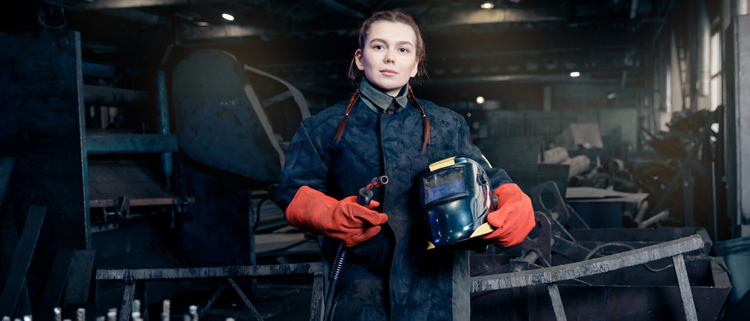 Worker girl with welding on steel structure in factory, light spark